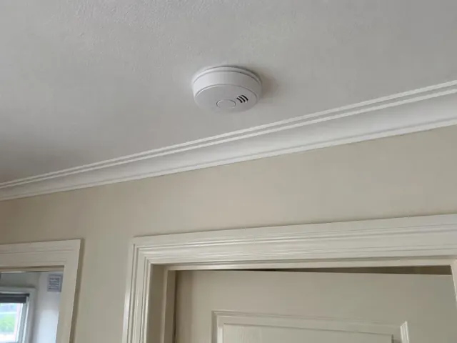 Ceiling smoke alarm above a doorway in a painted hallway with decorative trim in Maitland